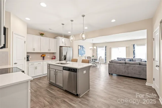 a large kitchen with stainless steel appliances kitchen island a stove a refrigerator a sink dishwasher and white cabinets with wooden floor