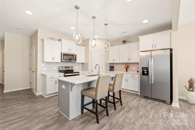 a kitchen with stainless steel appliances granite countertop a refrigerator a stove a sink dishwasher a dining table and chairs with wooden floor