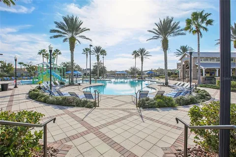 a view of swimming pool that has lawn chairs potted plants and palm trees