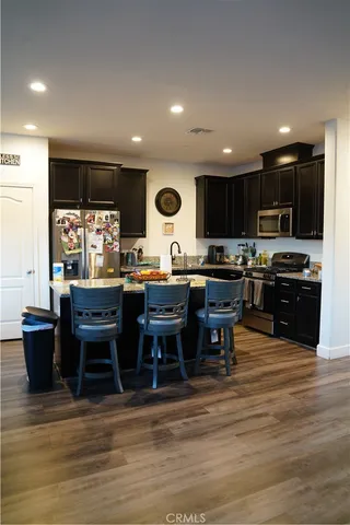 a kitchen with stainless steel appliances kitchen island granite countertop a stove top oven a sink dishwasher a dining table and chairs with wooden floor