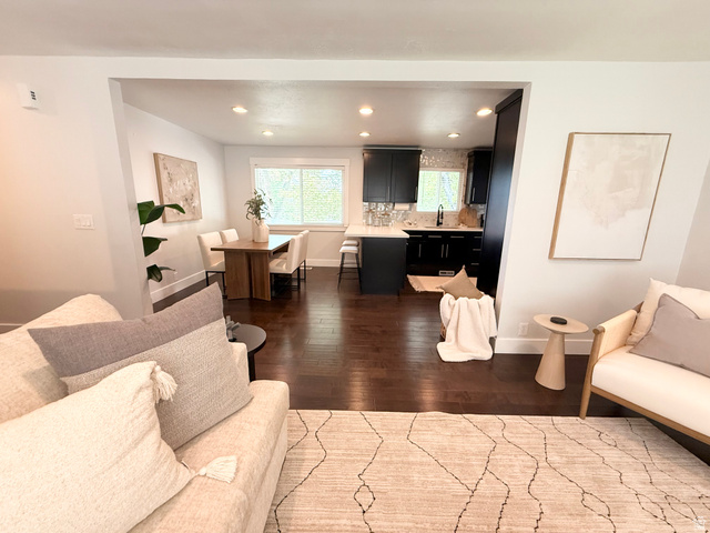 Hardwood flooring throughout, recessed lighting, and a kitchen featuring dark cabinetry, white countertops, and a tile backsplash
