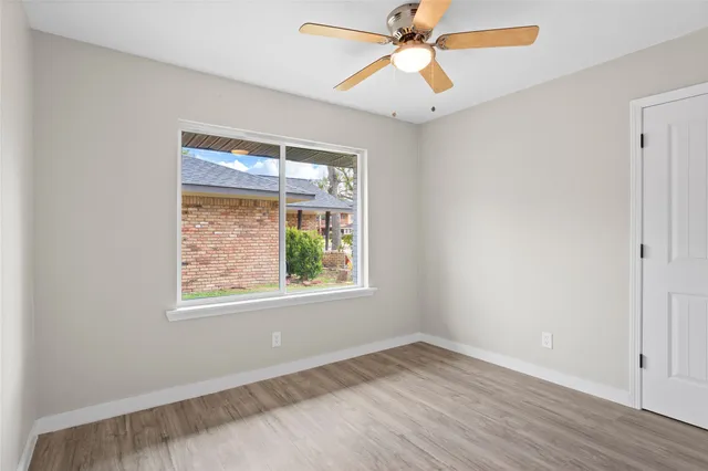 an empty room with wooden floor fan and windows