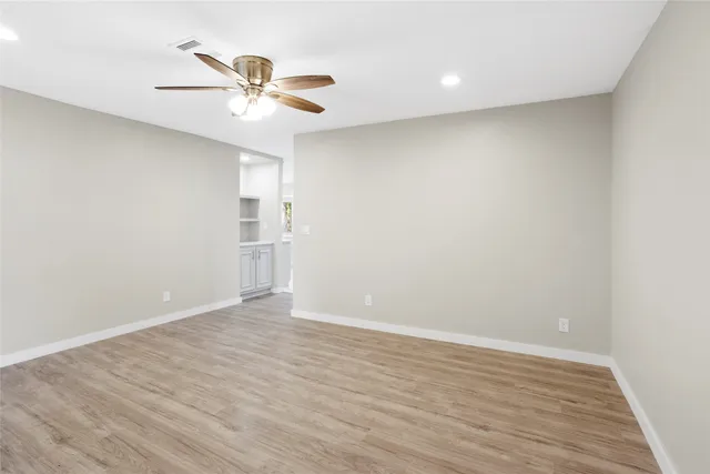 a view of an empty room with wooden floor and a ceiling fan
