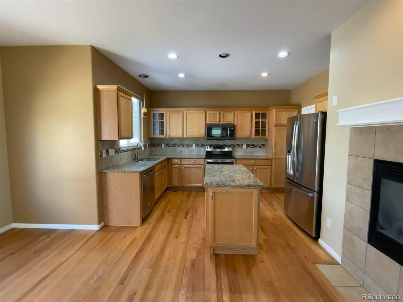 10838 Towerbridge Road Highlands Ranch, CO 80130 - Photo 3 of 26 a large kitchen with a center island wooden floor stainless steel appliances and cabinets