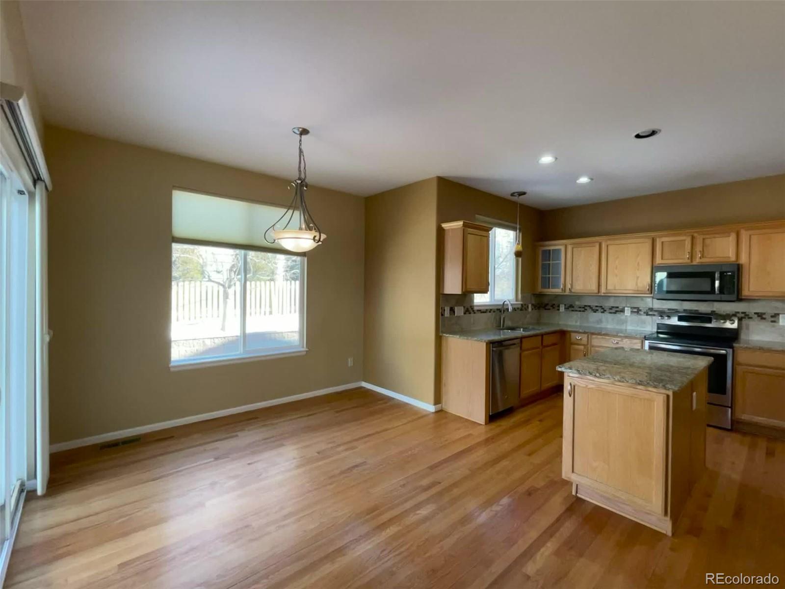 10838 Towerbridge Road Highlands Ranch, CO 80130 - Photo 4 of 26 a kitchen with granite countertop a stove top oven a sink dishwasher a refrigerator and a dining table with wooden floor