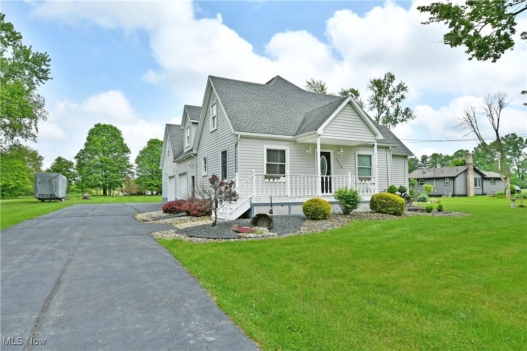 View of front facade featuring covered porch, a shingled roof, a front lawn, asphalt driveway, and a garage