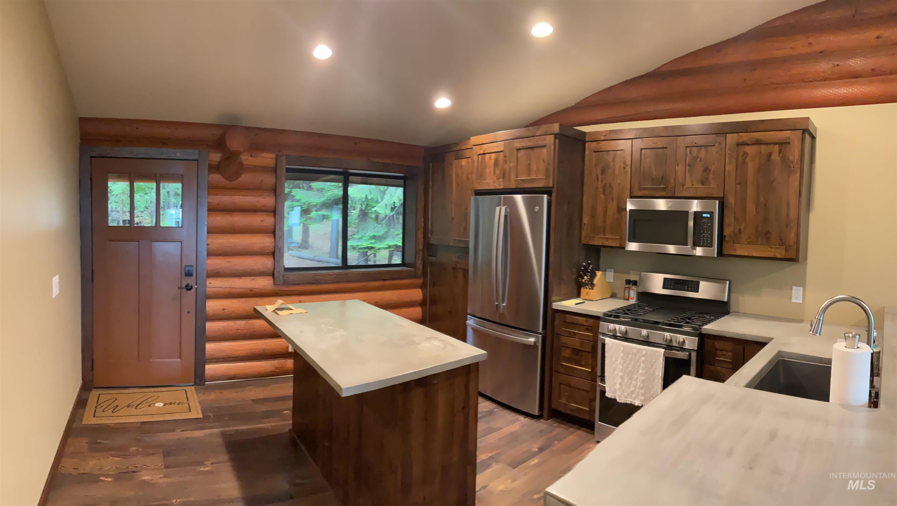 6125 Freeman Creek Road Lenore, ID 83541 - Photo 8 of 44 Kitchen featuring log wall accents, wood-finish flooring, a central island with a light-toned countertop, dark wood cabinetry, and stainless steel appliances