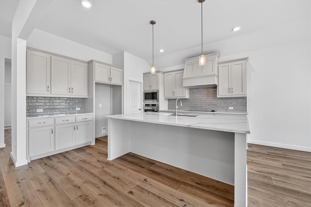 416 McAlpine Drive Springtown, TX 76082 - Photo 15 of 40 Gourmet kitchen featuring a large central island with a sink and pendant lighting, light-toned cabinetry, subway tile backsplash, and wood-finish flooring