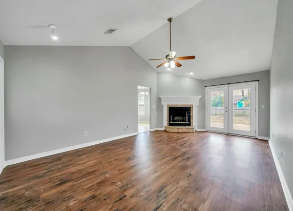 an empty room with wooden floor fireplace and ceiling fan