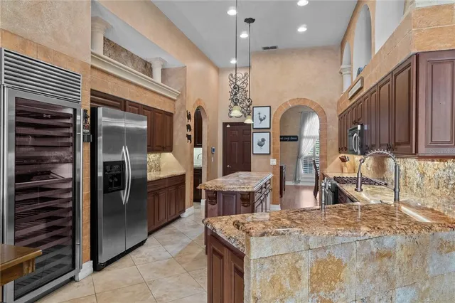 a kitchen with stainless steel appliances kitchen island granite countertop a refrigerator a stove and a sink with wooden cabinets