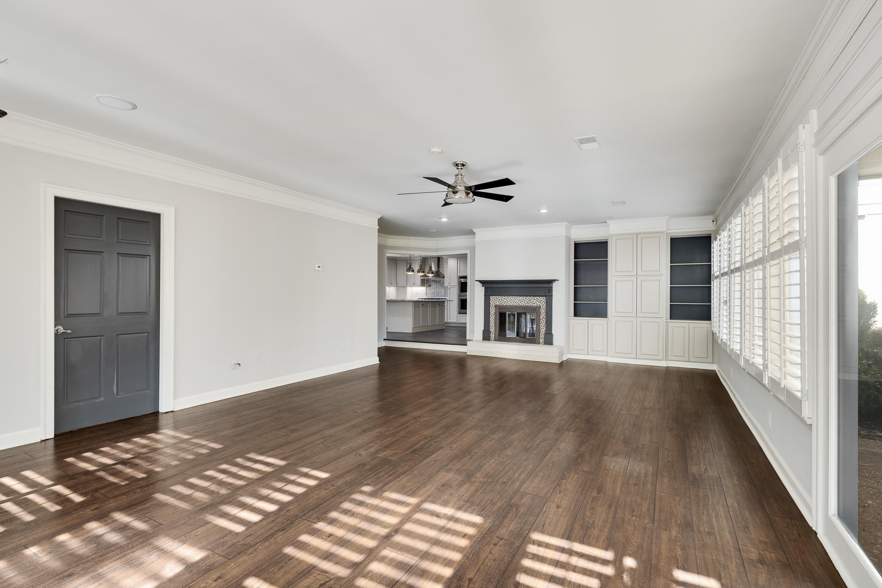 6867 River Birch Road Memphis, TN 38119 - Photo 21 of 40 Unfurnished living room featuring a glass covered fireplace, crown molding, dark wood-type flooring, a ceiling fan, and built in shelves