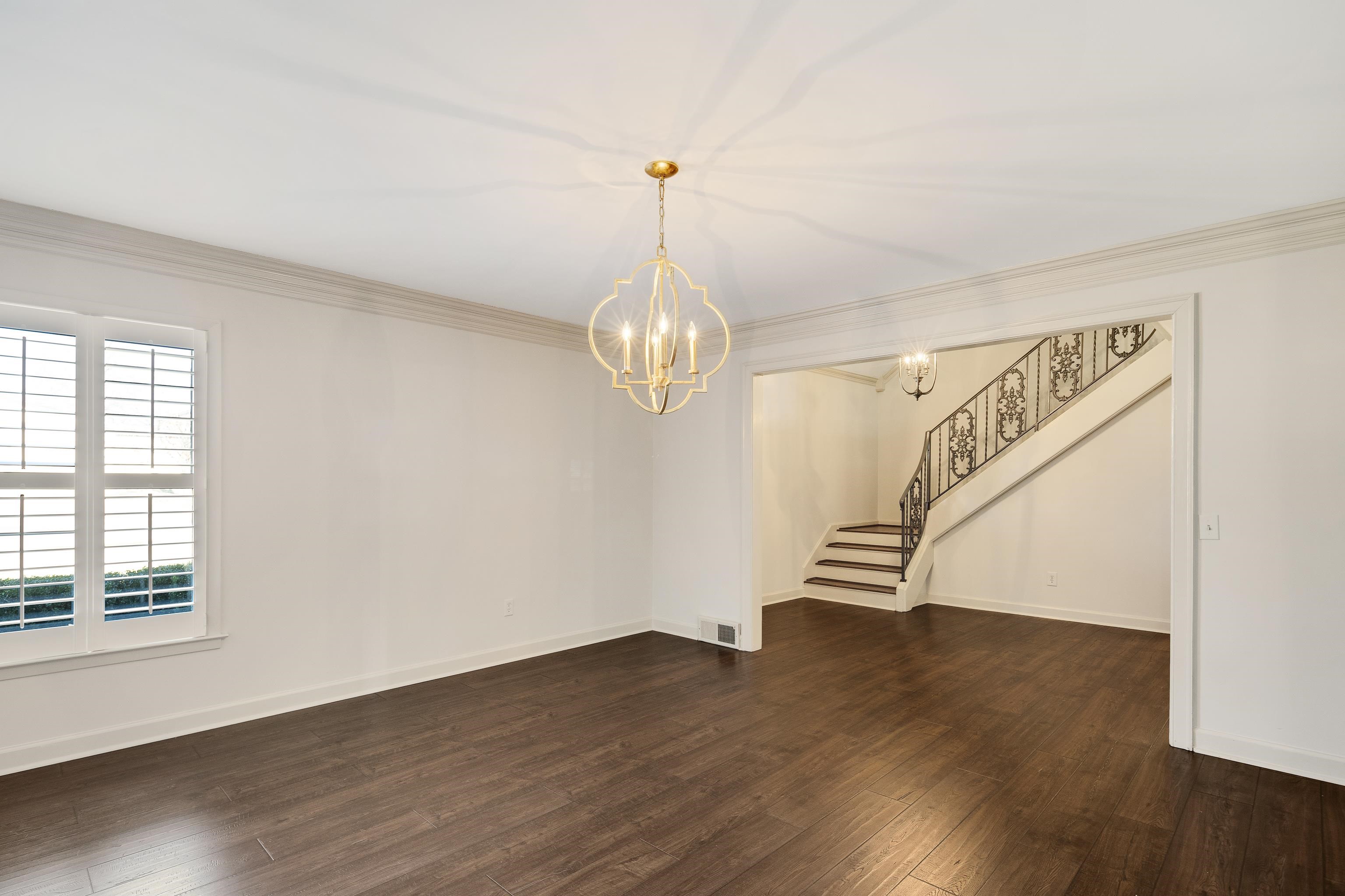 Unfurnished living room with stairway, dark wood-type flooring, a chandelier, and crown molding