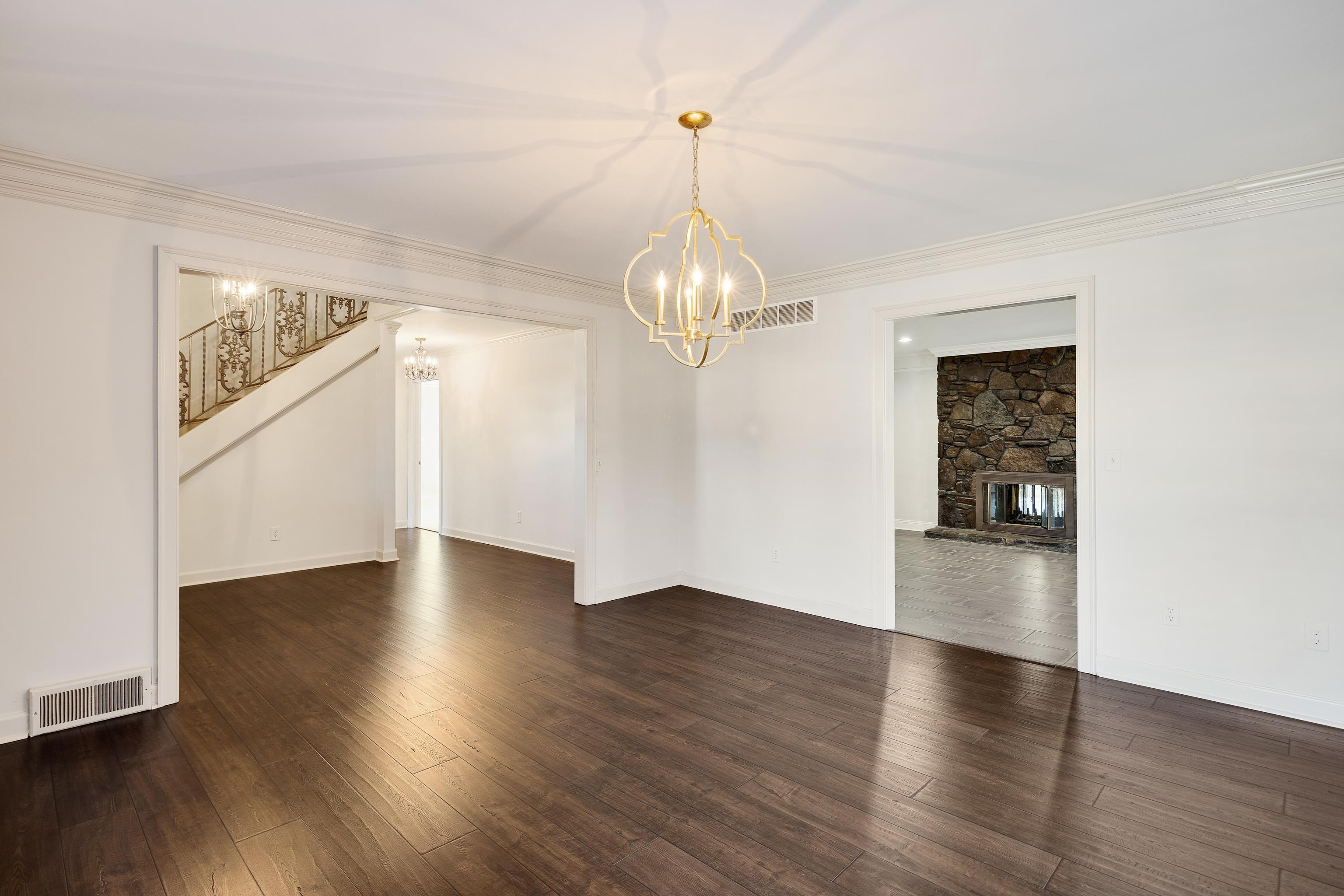 Unfurnished dining area with dark wood finished floors, a stone fireplace, stairway, a chandelier, and crown molding