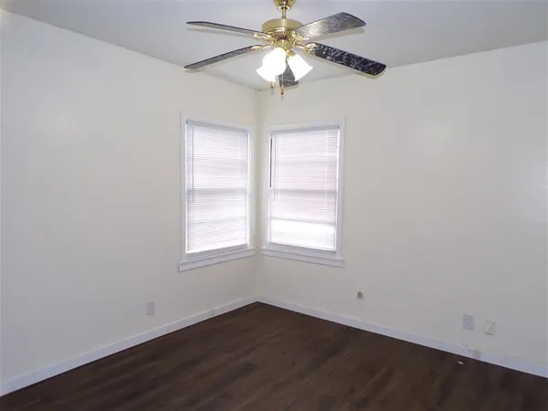 an empty room with wooden floor chandelier fan and windows
