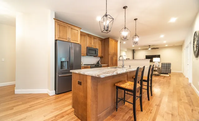 a kitchen with stainless steel appliances kitchen island granite countertop a kitchen island a stove a refrigerator a sink a dining table and chairs with wooden floor