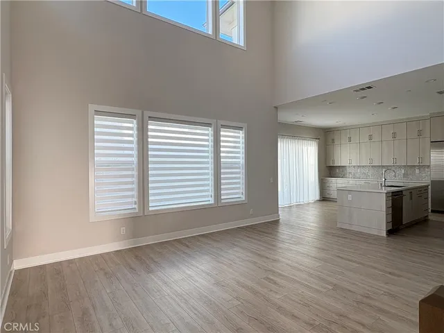 a view of an empty room with wooden floor and a kitchen