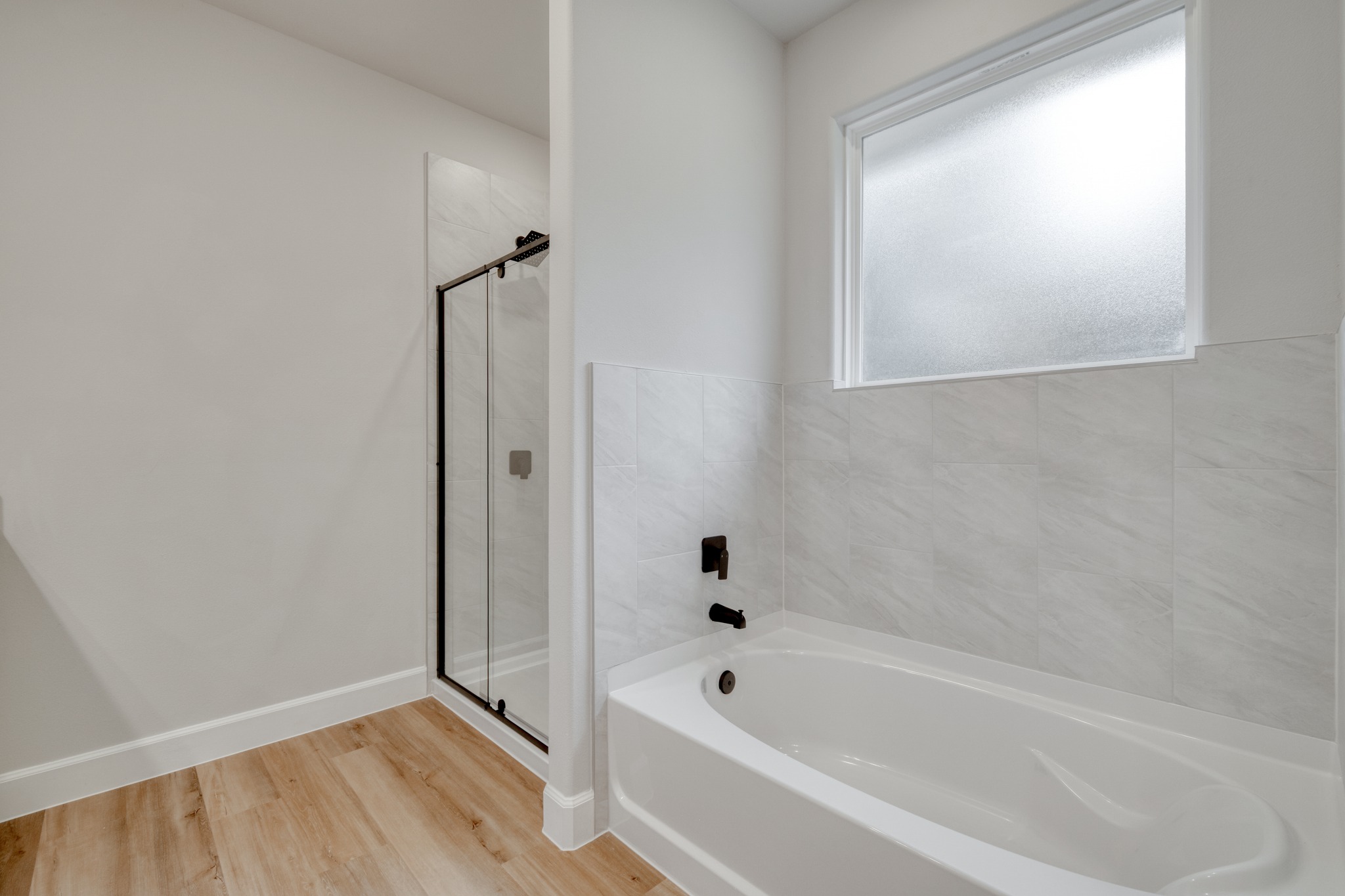 116 Pine Point Cove Elgin, TX 78621 - Photo 17 of 27 Bathroom featuring a white soaking tub with black fixtures, a shower with a black-framed glass enclosure, and wood-finish flooring