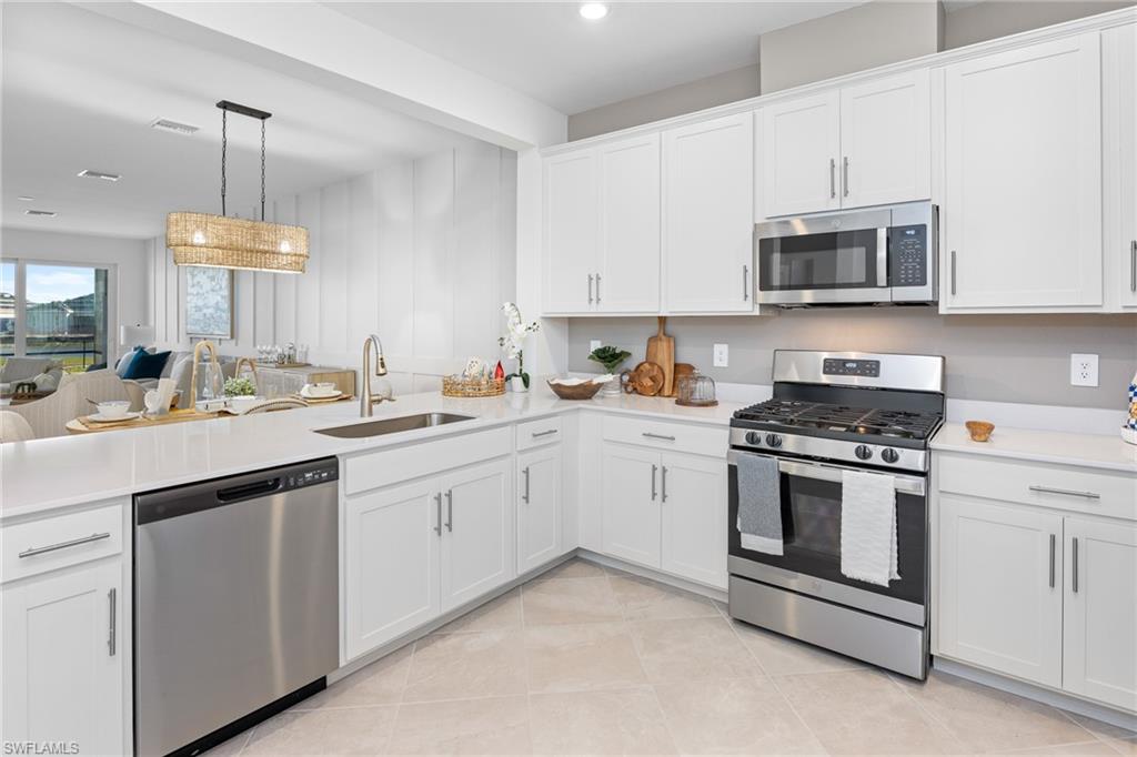 14888 Anchorage Road Punta Gorda, FL 33982 - Photo 10 of 34 Kitchen with appliances with stainless steel finishes, a peninsula, light countertops, light tile patterned floors, and white cabinetry