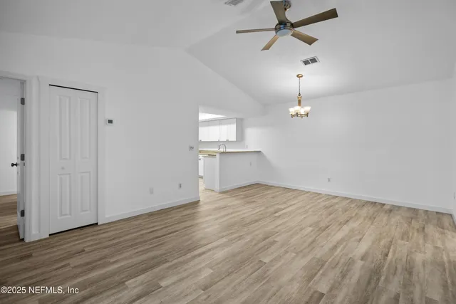 an empty room with wooden floor ceiling fan and windows