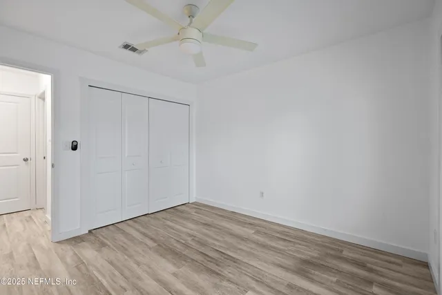 an empty room with wooden floor fan and windows