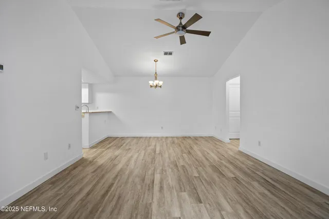 an empty room with wooden floor ceiling fan and windows
