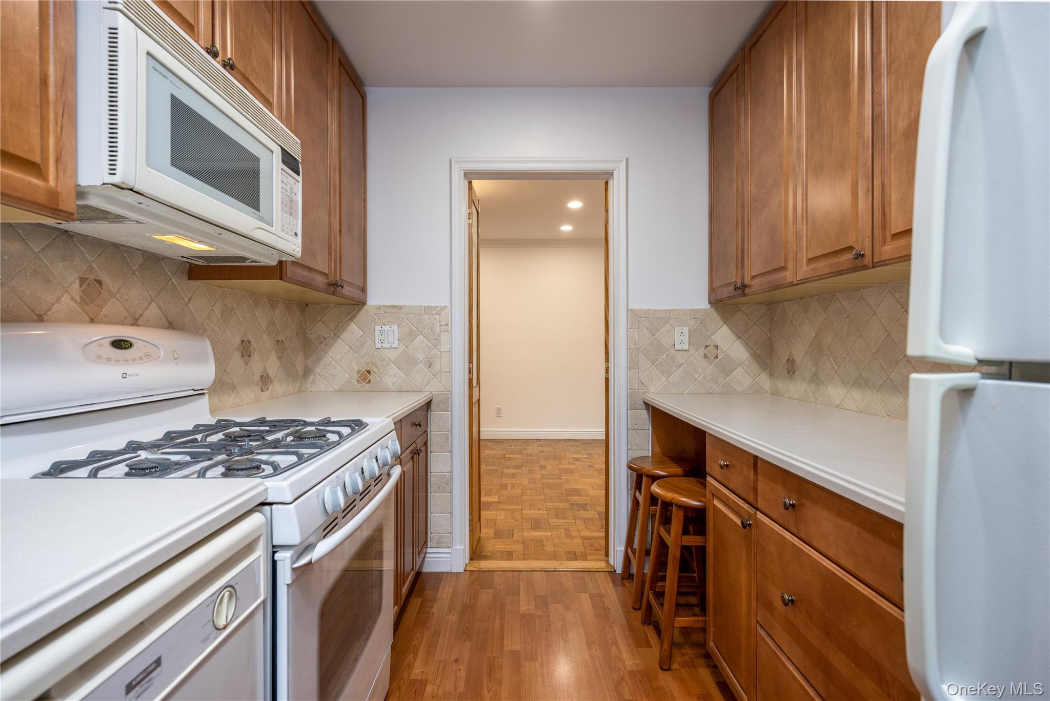 2303 Palmer Avenue, Unit F New Rochelle, NY 10801 - Photo 8 of 22 Kitchen with light countertops, brown cabinetry, light wood finished floors, white appliances, and backsplash