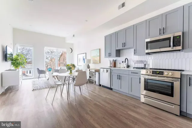 a kitchen with stainless steel appliances a white stove top oven a sink dishwasher a dining table and chairs with wooden floor