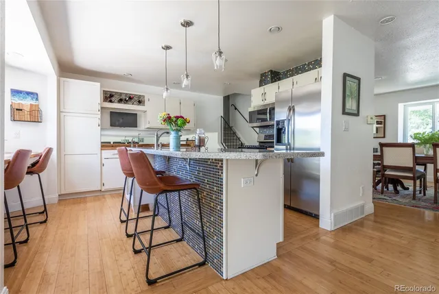 a kitchen with stainless steel appliances granite countertop a stove top oven a sink dishwasher a dining table and chairs with wooden floor