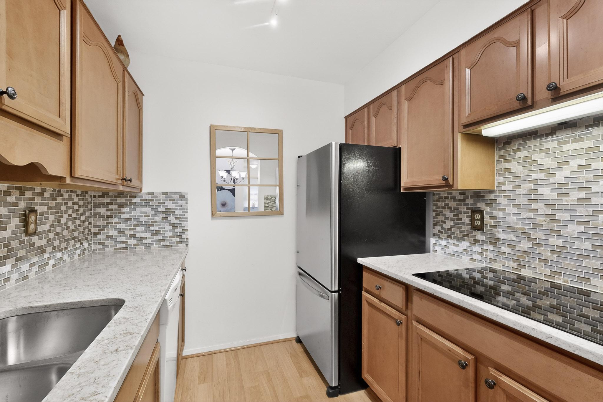 8210 Bent Tree Road, Unit 104 Austin, TX 78759 - Photo 11 of 39 Kitchen with light stone counters, freestanding refrigerator, light wood-type flooring, tasteful backsplash, and black electric stovetop