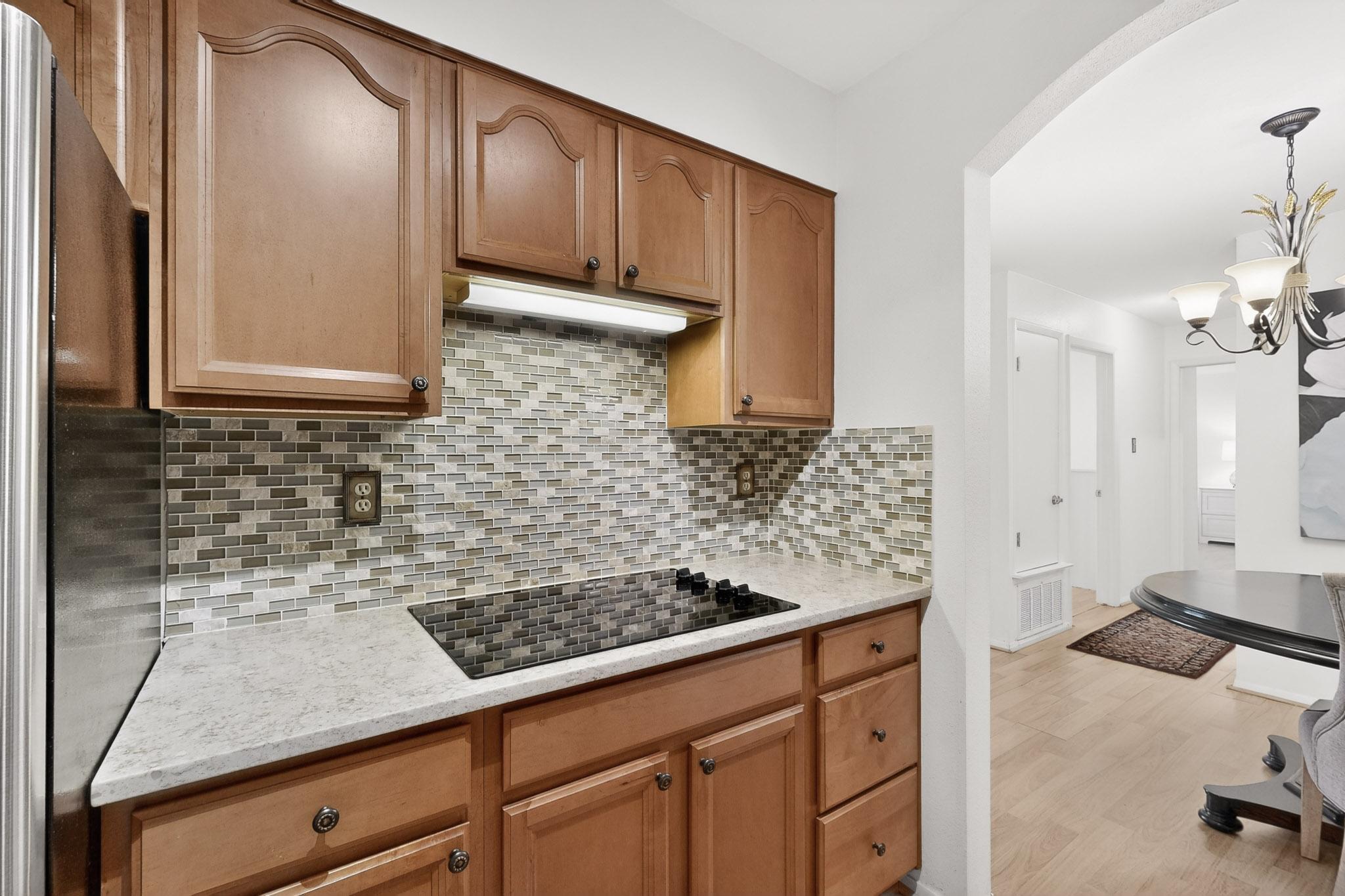 8210 Bent Tree Road, Unit 104 Austin, TX 78759 - Photo 13 of 39 Kitchen with freestanding refrigerator, light stone countertops, arched walkways, black electric cooktop, and wood finish cabinets