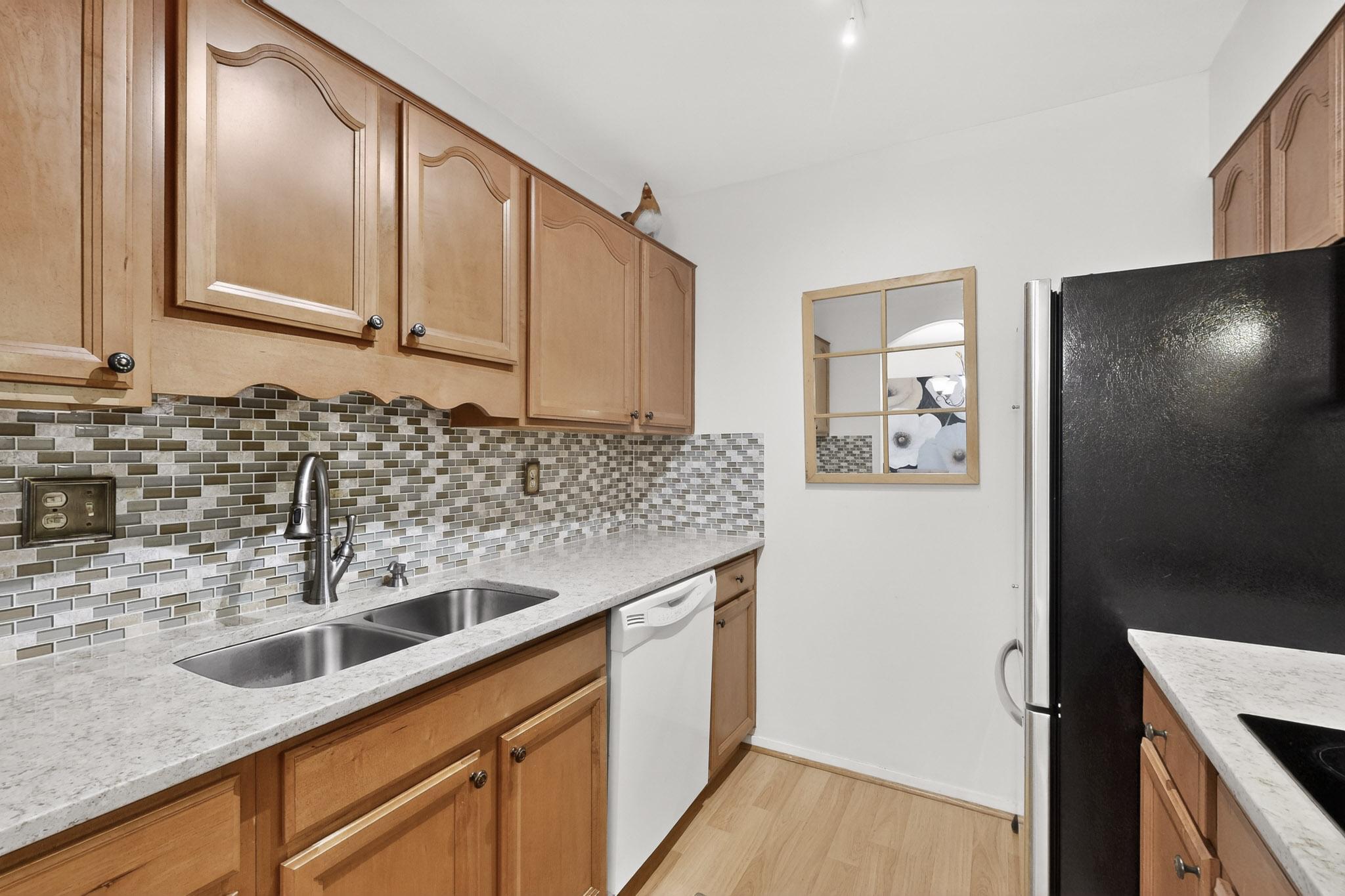 8210 Bent Tree Road, Unit 104 Austin, TX 78759 - Photo 10 of 39 Kitchen with black appliances, light stone counters, light wood finished floors, and backsplash