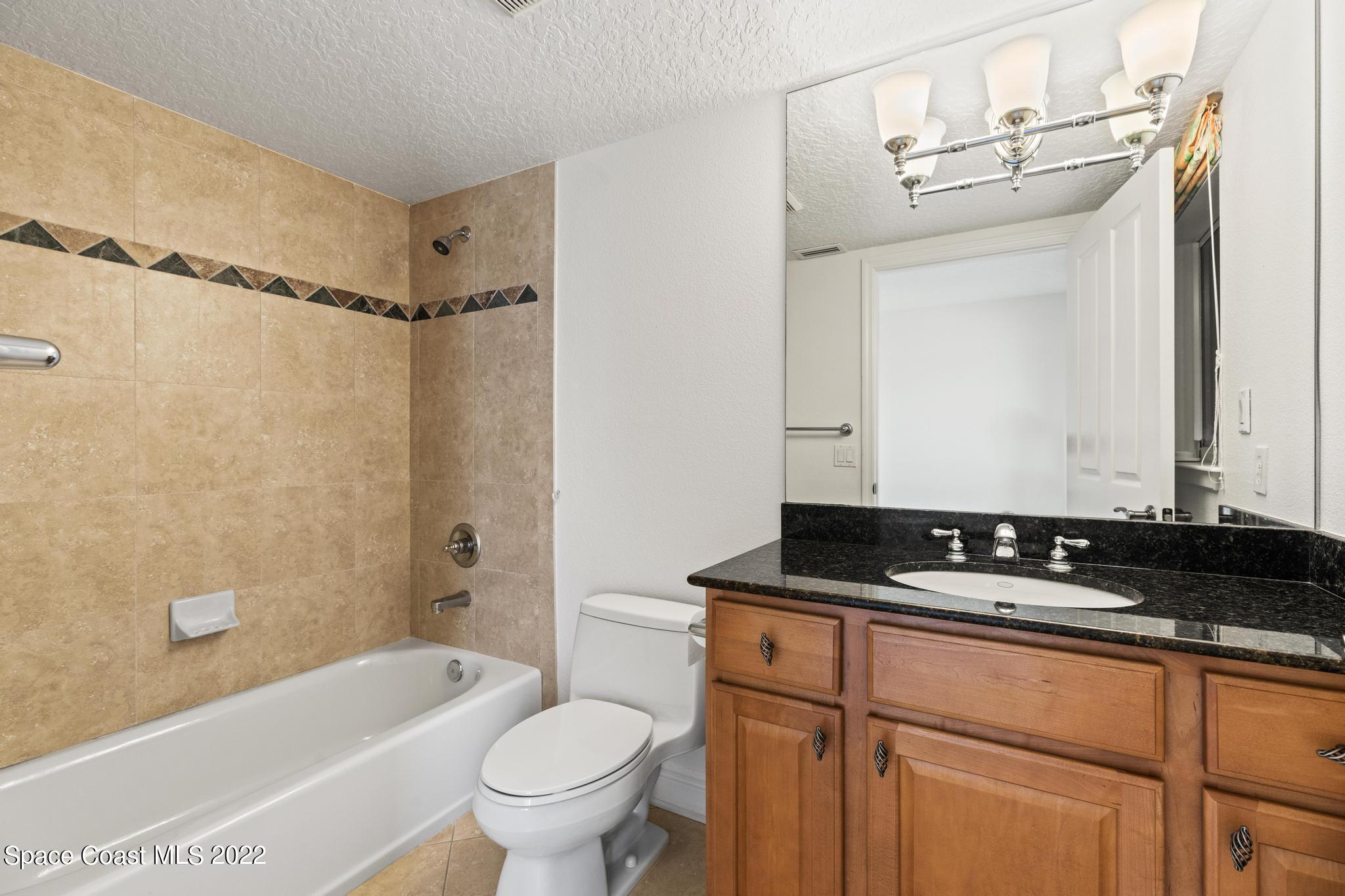 1095 Florida A1A, Unit 2301 Satellite Beach, FL 32937 - Photo 15 of 26 a bathroom with a granite countertop sink a toilet a mirror a bathtub and shower