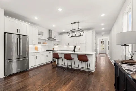 a kitchen with stainless steel appliances a stove a sink dishwasher a refrigerator and white cabinets with wooden floor