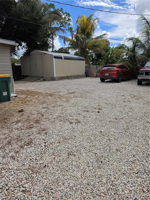 5230 Warren Street Naples, FL 34113 - Photo 5 of 22 Expansive gravel-covered lot featuring a large tan utility shed with a roll-up door