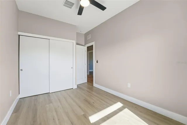 an empty room with wooden floor ceiling fan and windows