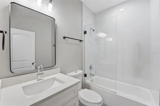 a bathroom with a bathtub shower sink vanity mirror and toilet