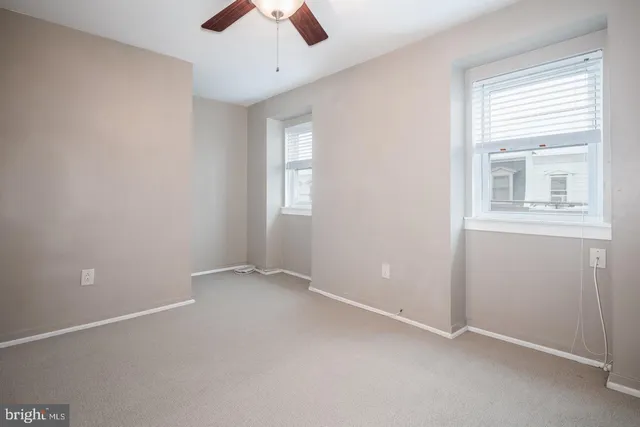 an empty room with chandelier fan and windows