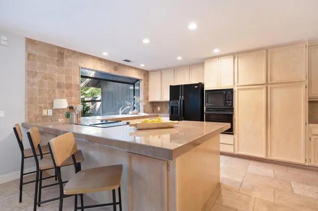 a kitchen with stainless steel appliances granite countertop a refrigerator a sink a stove a dining table and chairs