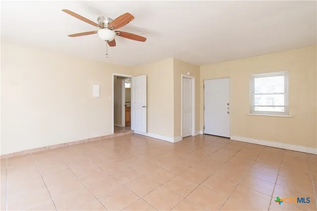 an empty room with chandelier fan and windows
