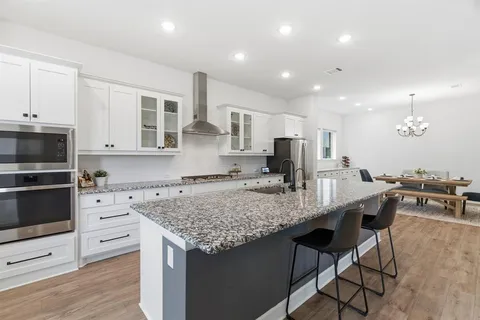 a kitchen with stainless steel appliances granite countertop a stove top oven a sink dishwasher a dining table and chairs with wooden floor