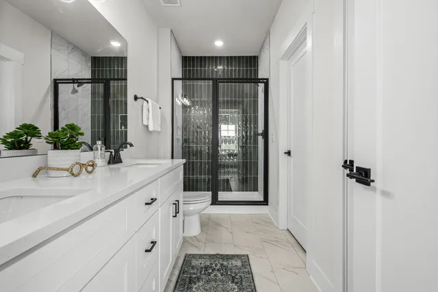 a bathroom with a double vanity sink a toilet a mirror and shower