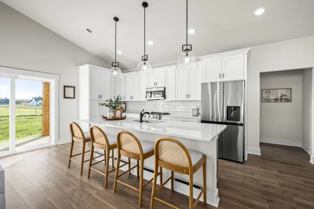 a kitchen with stainless steel appliances granite countertop a dining table chairs refrigerator and microwave