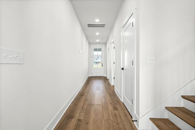 a view of a hallway with wooden floor and a bathroom
