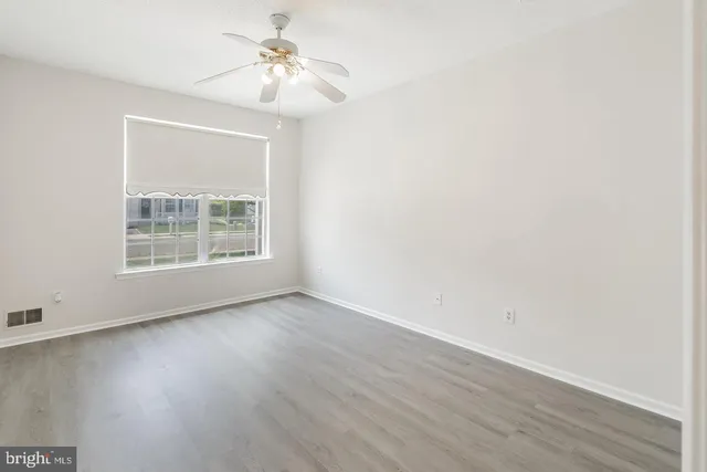 an empty room with wooden floor chandelier fan and windows