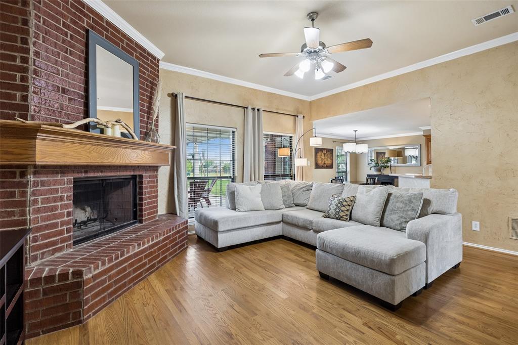 11211 Emerald Ranch Lane Forney, TX 75126 - Photo 15 of 35 Living area featuring a brick fireplace with a wood mantel, wood-finish flooring, crown molding, and a ceiling fan with integrated lighting
