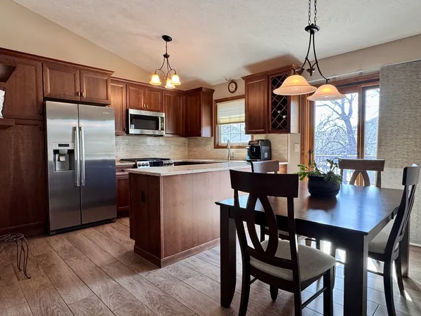 a kitchen with stainless steel appliances granite countertop a dining table chairs refrigerator and microwave