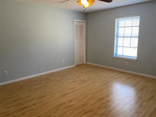 an empty room with wooden floor chandelier fan and windows