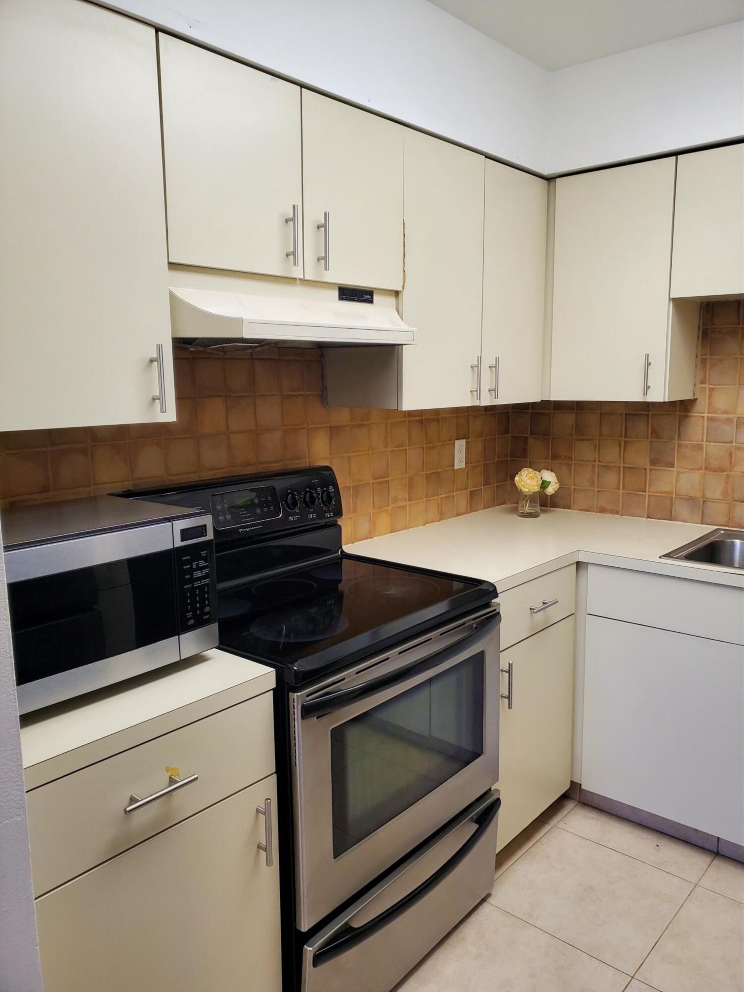 2445 Southwest 22nd Avenue, Unit 1020 Delray Beach, FL 33445 - Photo 13 of 37 a kitchen with granite countertop white cabinets and black appliances