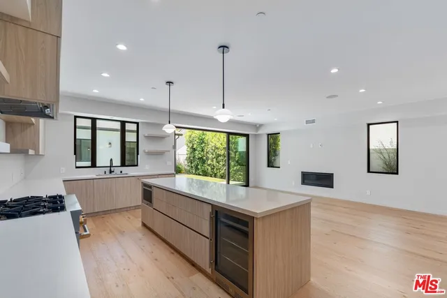 a large white kitchen with kitchen island a large counter top space a sink a window and stainless steel appliances