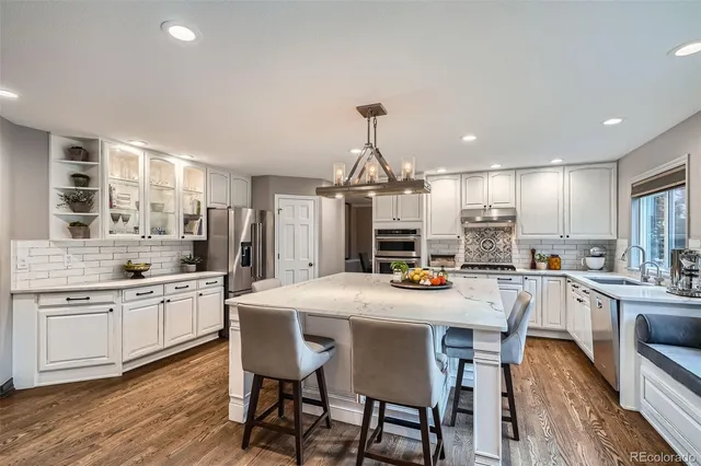 a kitchen with stainless steel appliances kitchen island granite countertop a dining table chairs stove refrigerator and cabinets